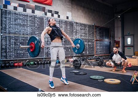 Young man watching woman lift barbell in gym View Large Photo Image Stock Photography - Young man watching woman lift barbell in gym. Fotosearch