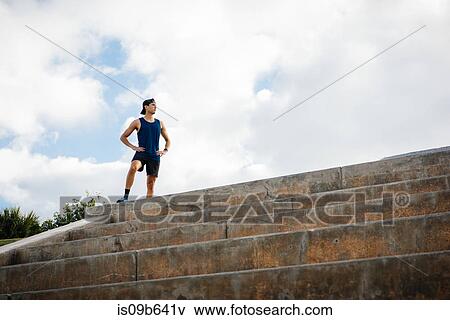 Stock Photo - Young man wearing sports clothing, standing at top of steps, hands on hips, South Point Park, Miami Beach, Florida, USA. Fotosearch