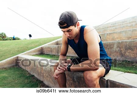 Young man wearing sports clothing, sitting on step, looking at activity tracker, South Point Park, Miami Beach, Florida, USA View Large Photo Image Stock Photograph - Young man wearing sports clothing, sitting on step, looking at activity tracker, South Point Park, Miami Beach, Florida, USA. Fotosearch