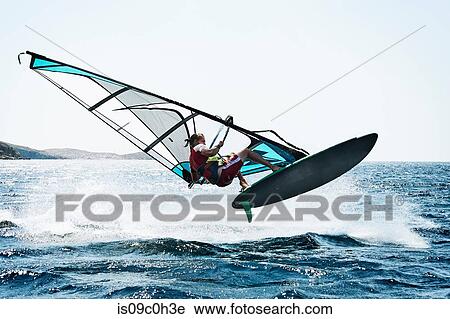 Stock Image - Young man windsurfing above ocean waves, Limnos, Khios, Greece. Fotosearch
