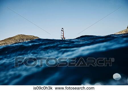 Stock Image - Young man windsurfing ocean waves, distant surface level view, Limnos, Khios, Greece. Fotosearch