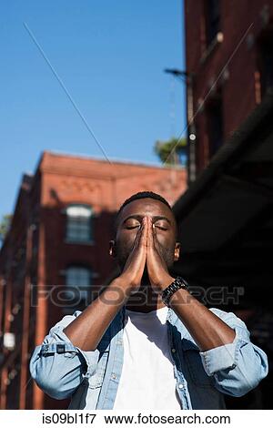 Stock Photo - Young man with palms together on face, New York, US. Fotosearch