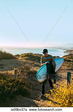 Stock Image - Young man with surfboard on beach, Morro Bay, California, United States. Fotosearch