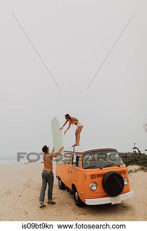 Young surfing couple unloading surfboard from top of recreational vehicle on beach, Jalama, Ventura, California, USA View Large Photo Image Picture - Young surfing couple unloading surfboard from top of recreational vehicle on beach, Jalama, Ventura, California, USA. Fotosearch