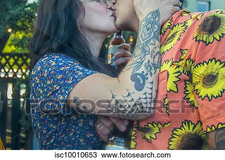 Young tattooed couple kissing each other at community garden party, cropped side view View Large Photo Image Stock Image - Young tattooed couple kissing each other at community garden party, cropped side view. Fotosearch