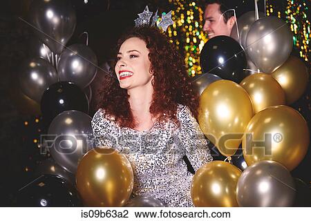 Stock Image - Young woman at party, surrounded by balloons. Fotosearch