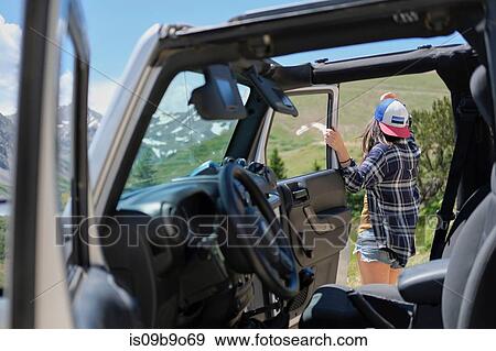 Stock Photo - Young woman by off road vehicle looking out over Rocky Mountains, Breckenridge, Colorado, USA. Fotosearch