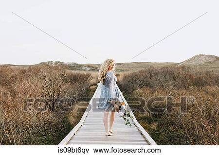 Young woman carrying bunch of flowers on coastal dune boardwalk, Menemsha, Martha's Vineyard, Massachusetts, USA View Large Photo Image Stock Photo - Young woman carrying bunch of flowers on coastal dune boardwalk, Menemsha, Martha's Vineyard, Massachusetts, USA. Fotosearch