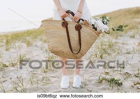 Stock Photo - Young woman carrying shoulder bag with flowers on coastal dunes, waist down, Menemsha, Martha's Vineyard, Massachusetts, USA. Fotosearch