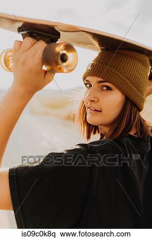 Stock Photography - Young woman carrying skateboard on her head on rural road, portrait, Exeter, California, USA. Fotosearch