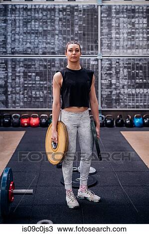 Young woman carrying weight plates in gym View Large Photo Image Stock Image - Young woman carrying weight plates in gym. Fotosearch