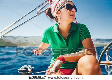 Stock Photo - Young woman crouching on yacht near coast, Croatia. Fotosearch
