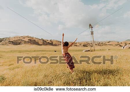 Stock Image - Young woman dancing in field landscape, rear view, Exeter, California, USA. Fotosearch