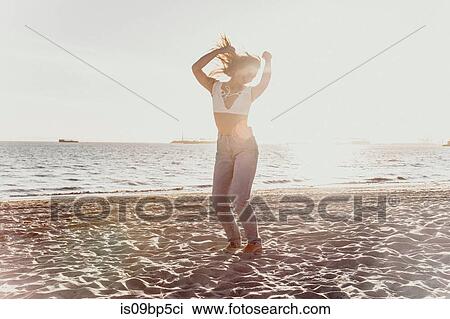 Stock Image - Young woman dancing on beach. Fotosearch