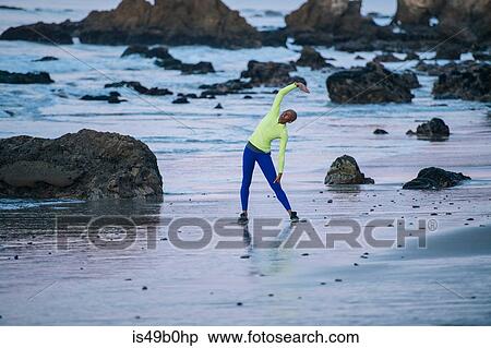 Stock Photography - Young woman exercising, stretching, on beach. Fotosearch
