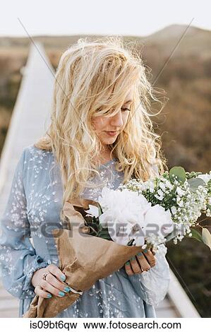 Young woman gazing at bunch of flowers on coastal dune boardwalk, Menemsha, Martha's Vineyard, Massachusetts, USA View Large Photo Image Stock Photo - Young woman gazing at bunch of flowers on coastal dune boardwalk, Menemsha, Martha's Vineyard, Massachusetts, USA. Fotosearch