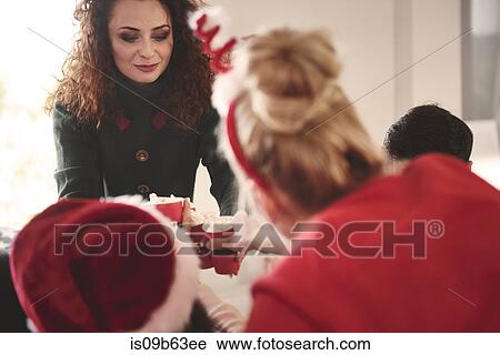 Stock Image - Young woman handing out popcorn at christmas party. Fotosearch