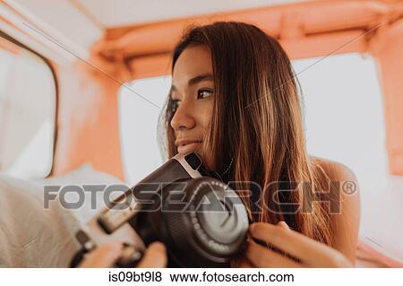 Stock Photo - Young woman holding up instant camera in back of recreational vehicle, Jalama, California, USA. Fotosearch