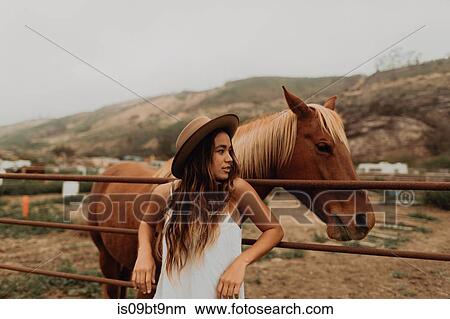 Young woman in felt hat leaning against fence next to horse, Jalama, California, USA View Large Photo Image Picture - Young woman in felt hat leaning against fence next to horse, Jalama, California, USA. Fotosearch