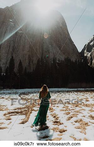 Young woman in long dress standing in sunlit snow covered mountain landscape, rear view, Yosemite Village, California, USA View Large Photo Image Stock Photography - Young woman in long dress standing in sunlit snow covered mountain landscape, rear view, Yosemite Village, California, USA. Fotosearch