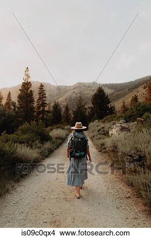 Young woman in maxi dress wearing backpack walking along rural road, rear view, Mineral King, California, USA View Large Photo Image Picture - Young woman in maxi dress wearing backpack walking along rural road, rear view, Mineral King, California, USA. Fotosearch