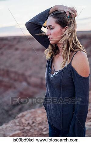 Stock Image - Young woman in remote setting, looking at view, holding hair off face, Mexican Hat, Utah, USA. Fotosearch