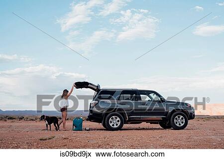 Young woman in remote setting, opening boot of SUV, dog beside her, Mexican Hat, Utah, USA View Large Photo Image Stock Photo - Young woman in remote setting, opening boot of SUV, dog beside her, Mexican Hat, Utah, USA. Fotosearch