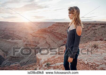Stock Photo - Young woman in remote setting, standing on cliff edge, looking at view, rear view, Mexican Hat, Utah, USA. Fotosearch