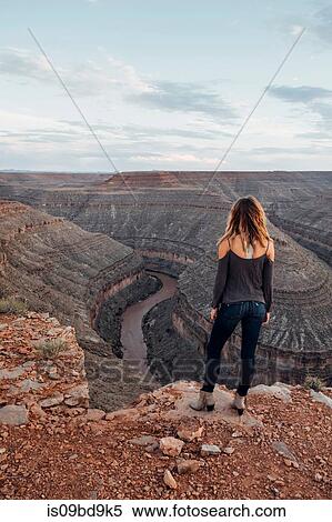 Stock Photography - Young woman in remote setting, standing on cliff edge, looking at view, rear view, Mexican Hat, Utah, USA. Fotosearch