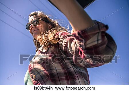 Stock Image - Young woman in sunglasses against blue sky, low angle view. Fotosearch