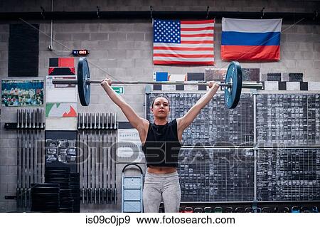 Stock Photo - Young woman lifting barbell in gym. Fotosearch