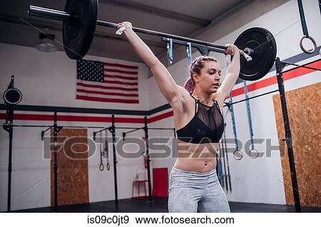 Stock Photo - Young woman lifting barbell in gym. Fotosearch