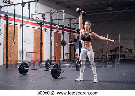 Young woman lifting dumbbell with one arm in gym View Large Photo Image Stock Image - Young woman lifting dumbbell with one arm in gym. Fotosearch