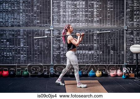 Picture - Young woman lifting weight bar in gym. Fotosearch