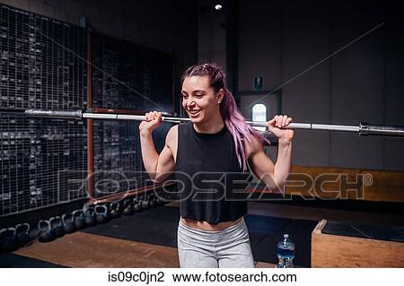 Young woman lifting weight bar in gym View Large Photo Image Stock Image - Young woman lifting weight bar in gym. Fotosearch