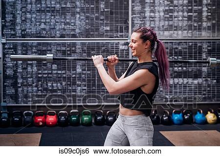 Stock Photograph - Young woman lifting weight bar in gym. Fotosearch