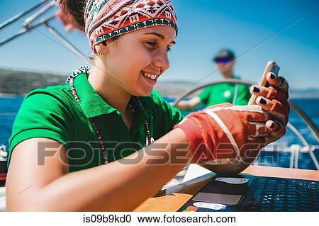 Stock Image - Young woman looking at smartphone aboard yacht near coast, Croatia. Fotosearch