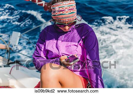Stock Image - Young woman looking at smartphone aboard yacht, Croatia. Fotosearch