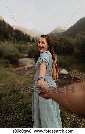 Stock Photo - Young woman looking back and leading boyfriend by hand at rural river, Mineral King, California, USA. Fotosearch