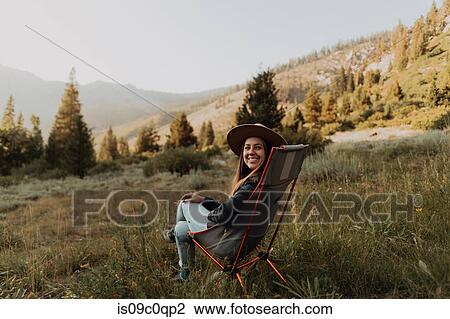 Stock Image - Young woman looking back from deck chair in rural valley, portrait, Mineral King, California, USA. Fotosearch