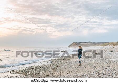 Stock Photo - Young woman looking out to sea from windy beach, Menemsha, Martha's Vineyard, Massachusetts, USA. Fotosearch