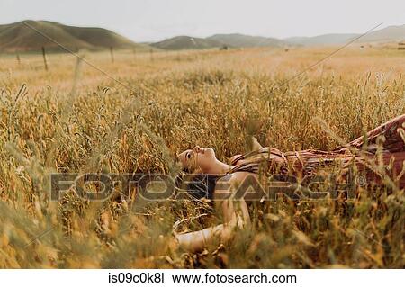 Stock Image - Young woman lying in field of long grass, Exeter, California, USA. Fotosearch