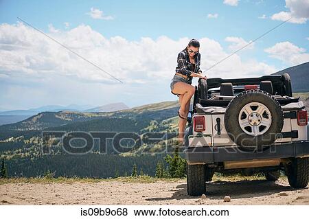 Stock Photo - Young woman on road trip climbing into parked off road vehicle, Breckenridge, Colorado, USA. Fotosearch