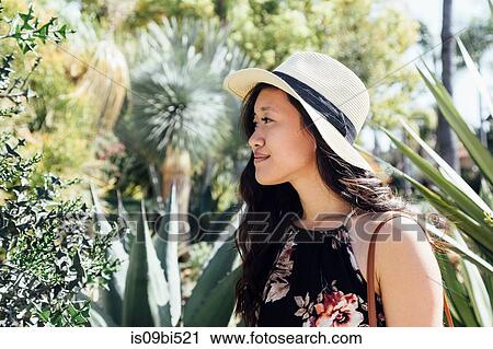 Stock Image - Young woman outdoors, looking at plants in garden. Fotosearch