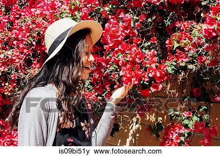 Stock Photo - Young woman outdoors, looking at colourful hanging flowers. Fotosearch