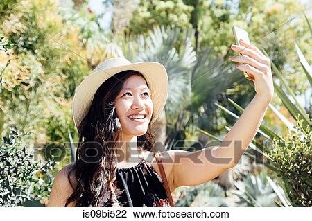 Stock Image - Young woman outdoors, taking selfie in ornamental garden. Fotosearch