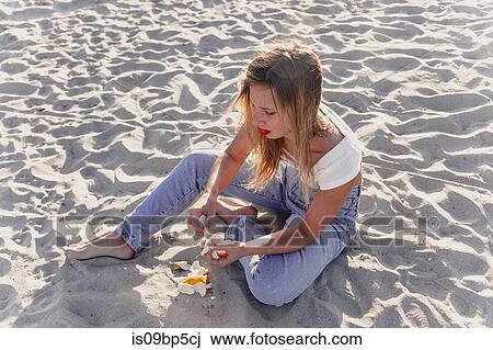 Stock Image - Young woman peeling fruit on beach. Fotosearch