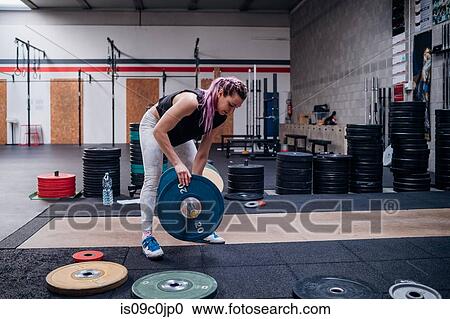 Stock Image - Young woman placing weight plate into bar in gym. Fotosearch