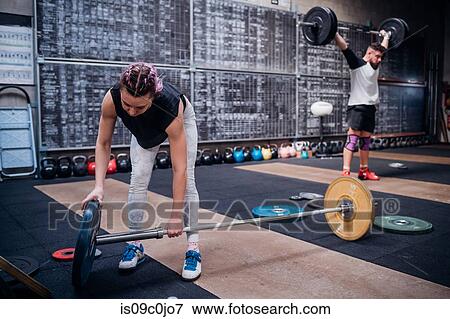 Young woman placing weight plate into bar in gym View Large Photo Image Stock Photo - Young woman placing weight plate into bar in gym. Fotosearch