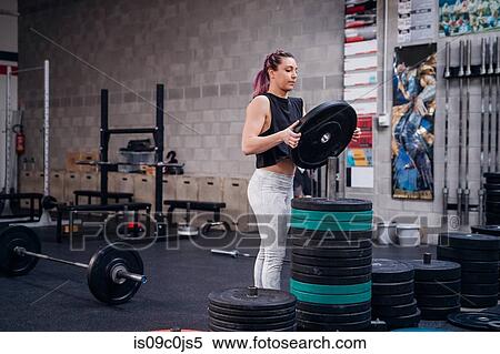 Young woman placing weight plate onto rack in gym View Large Photo Image Stock Photography - Young woman placing weight plate onto rack in gym. Fotosearch
